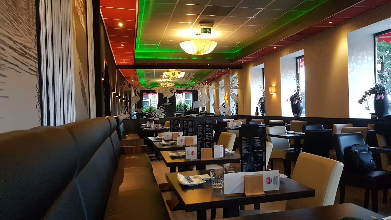 De zaal van De Lange Muur in de avond, met groen en rood licht in het plafond en een lange bank langs de muur